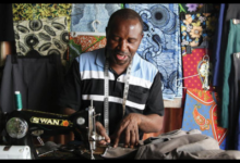 Black male tailor sewing with singer machine with fabric in the background